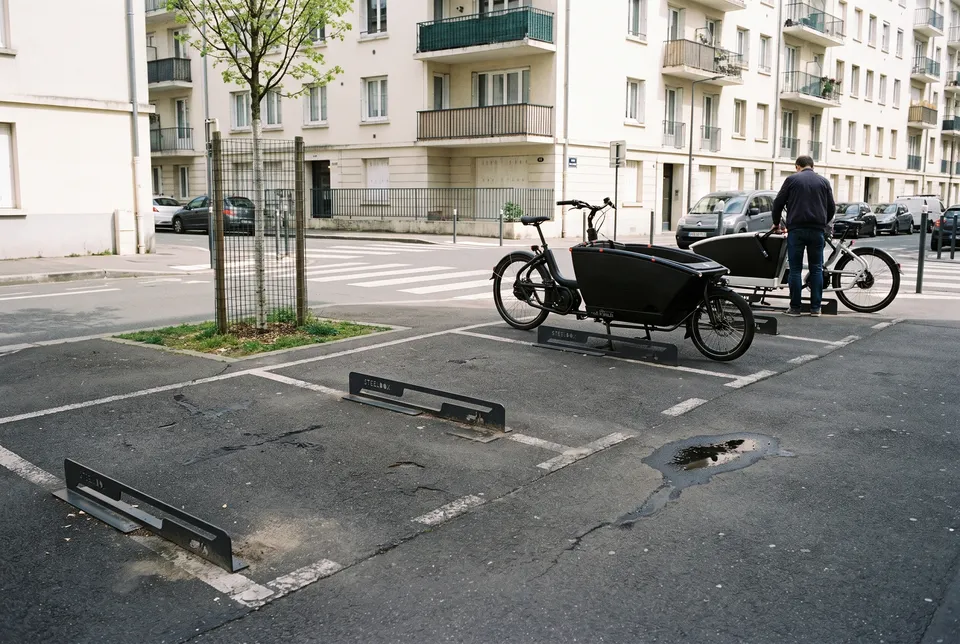 Arceaux vélo cargo Cargotek en acier anthracite, à profil bas, sur des places de stationnement en ville avec deux vélos cargo garés