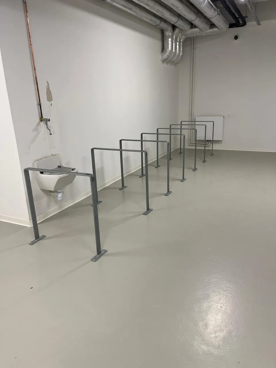 Arceaux vélo Recto en acier galvanisé sur platines, alignés dans le local vélo d'une université