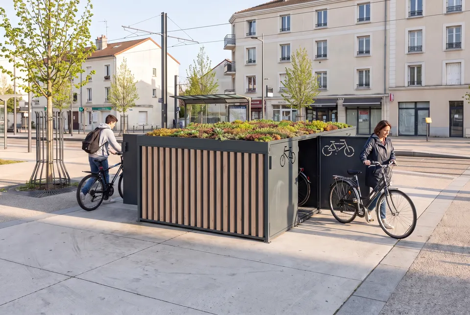 Box vélo sécurisé Dualis à bardage bois et toiture végétalisée en sedum, sur une place près d'un arrêt de tramway