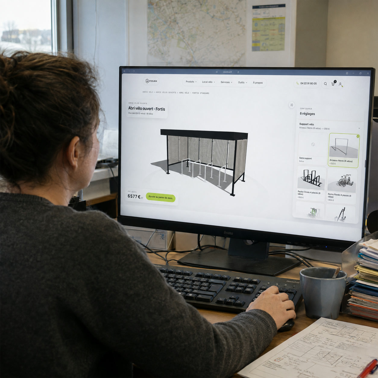 Utilisatrice configurant un abri vélo ouvert Fortis dans le configurateur 3D Steelbox depuis son poste de travail, pré-devis affiché à 6 577 € HT